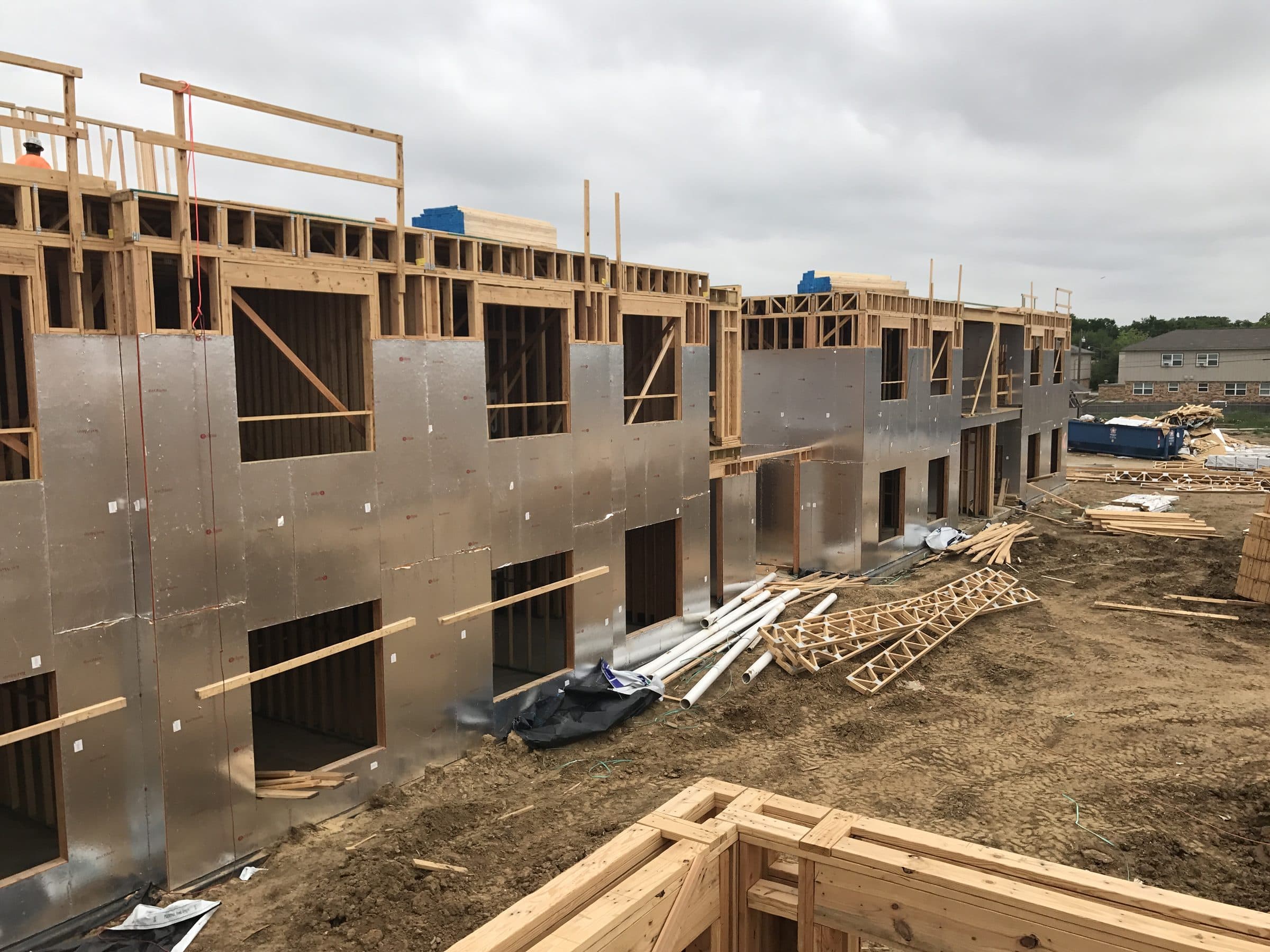 Wood framing with foil-faced sheathing going up, a worker on the top plate
