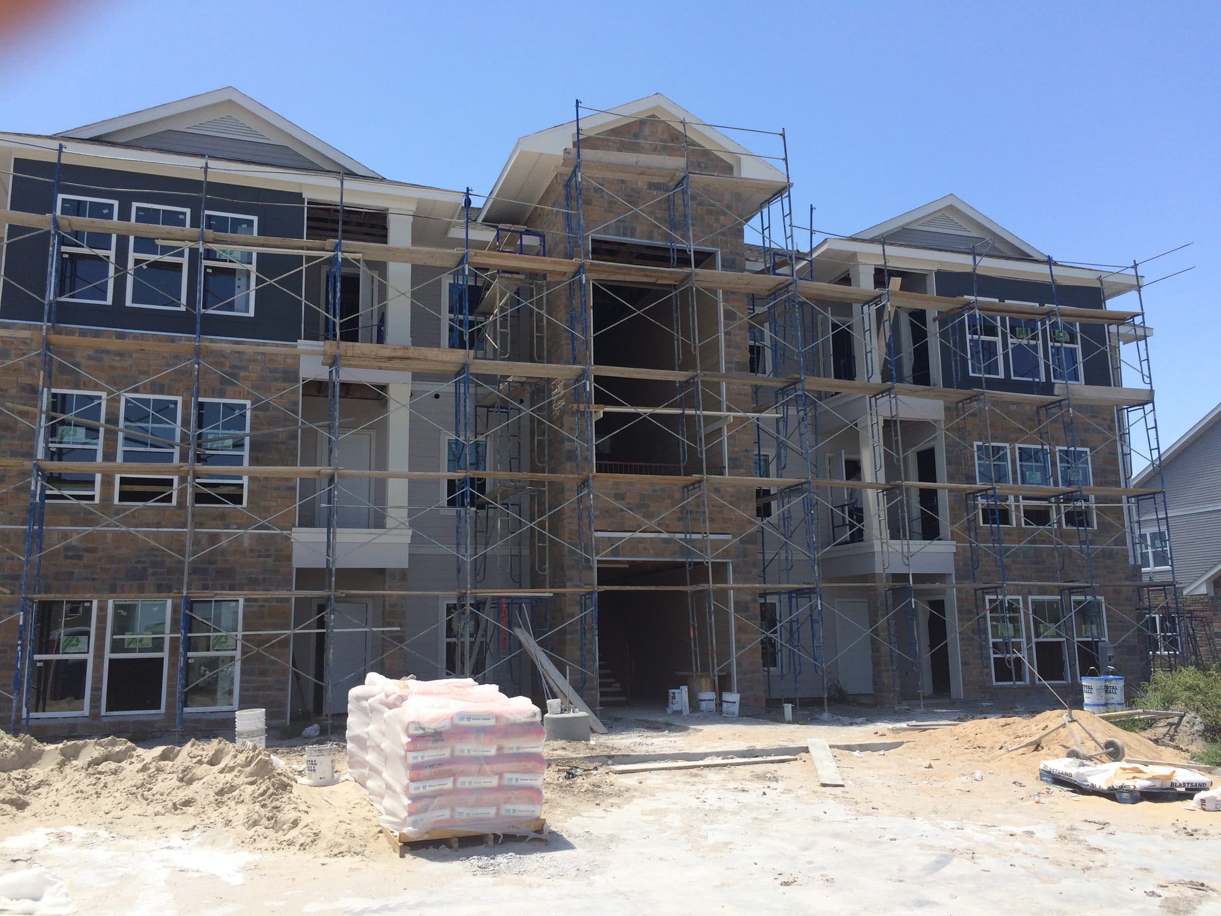 A three-story building wrapped in scaffolding, stone veneer going up